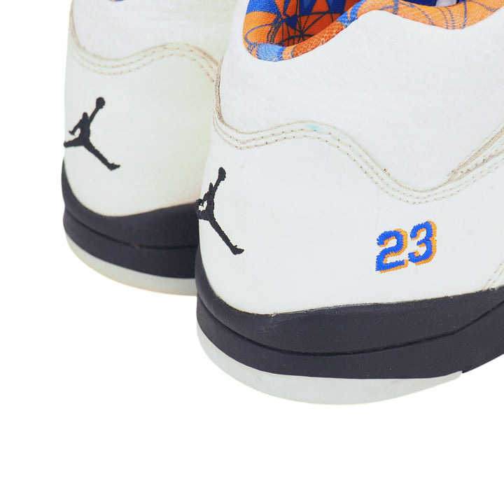 Close-up of the heel of a pair of white Jordan 5 sneaker with black Jumpman logo and blue and orange '23' on a white background