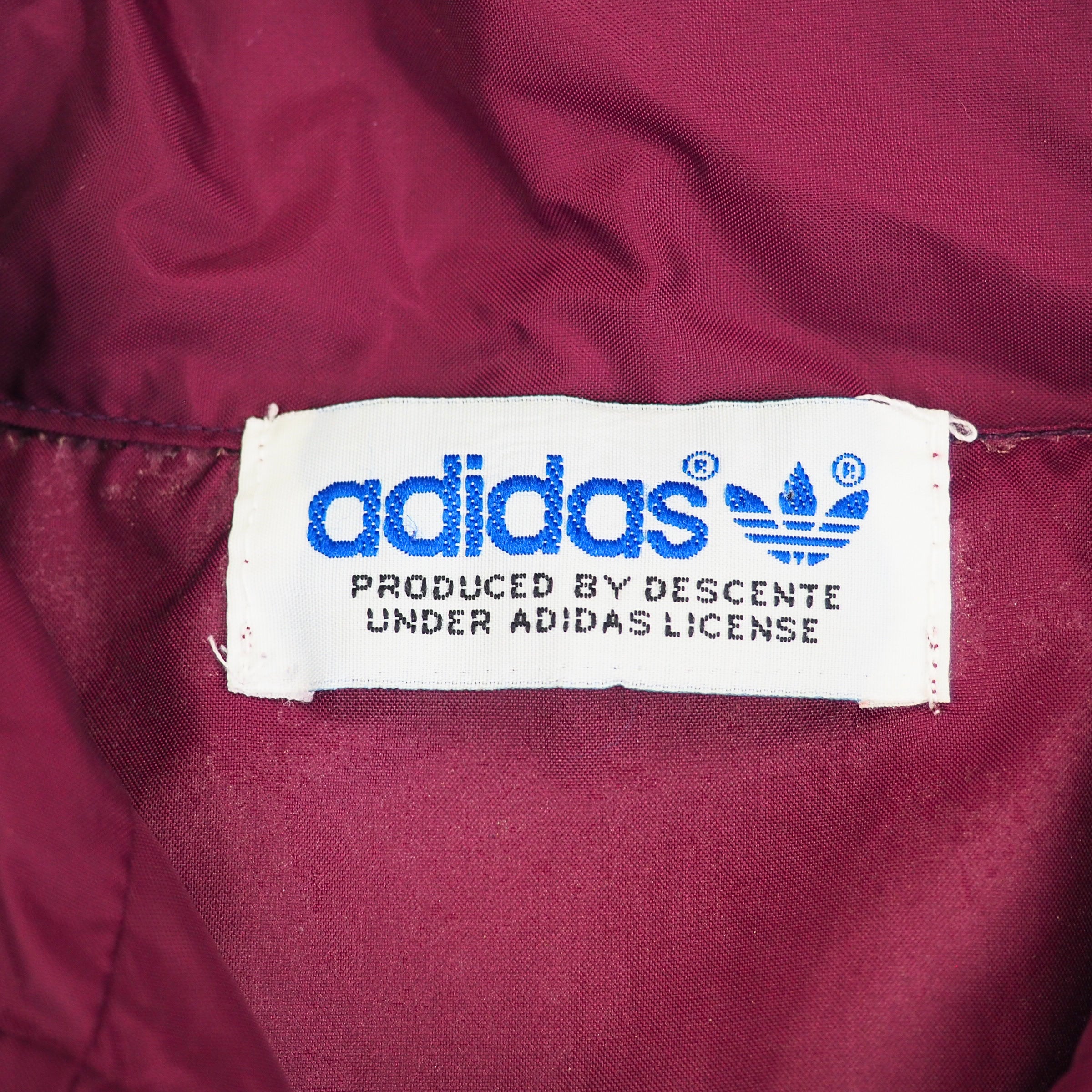 Close-up of an Adidas by Descente label on a maroon fabric background