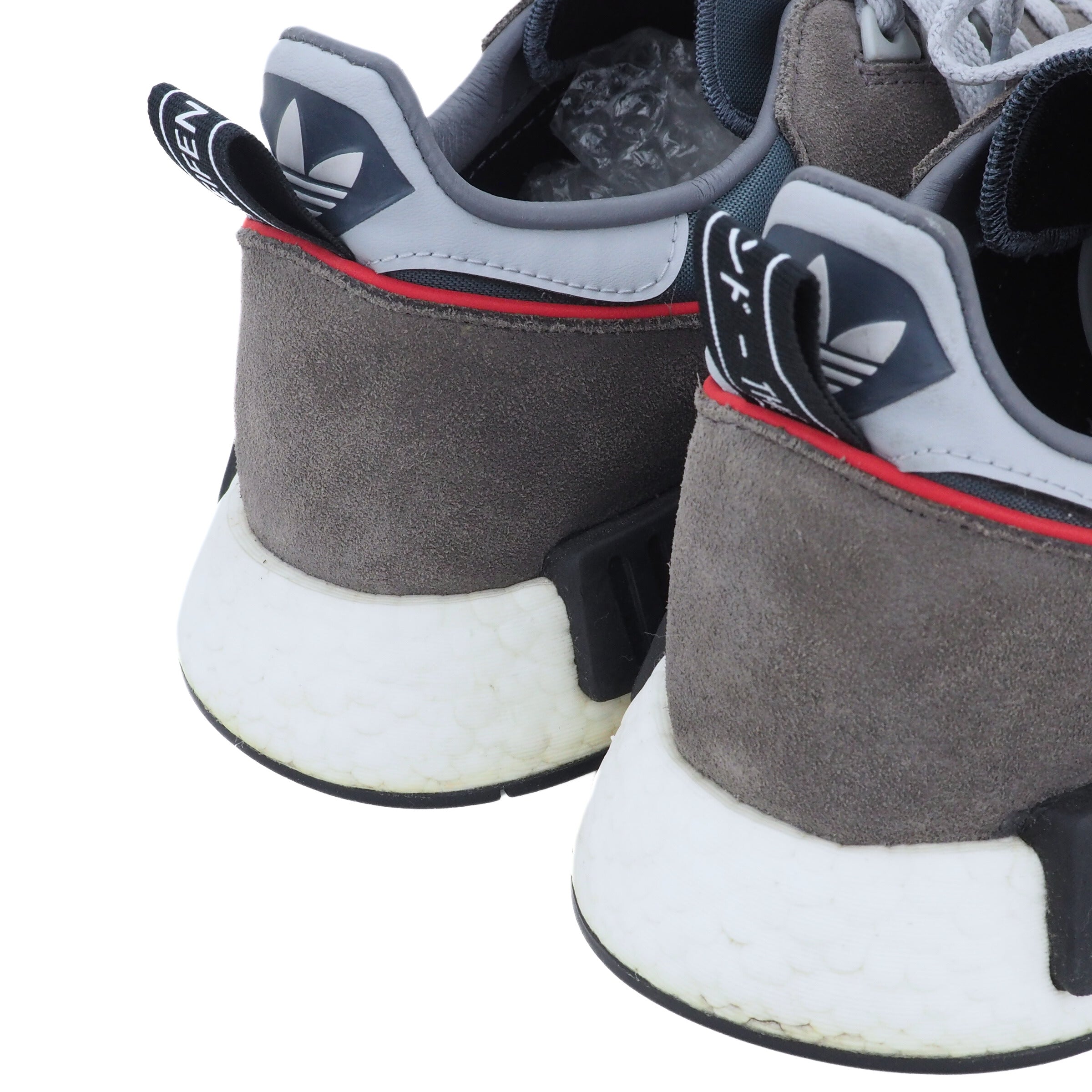 Close up of the heels of a pair of gray and white Adidas sneakers with red accents on a white background