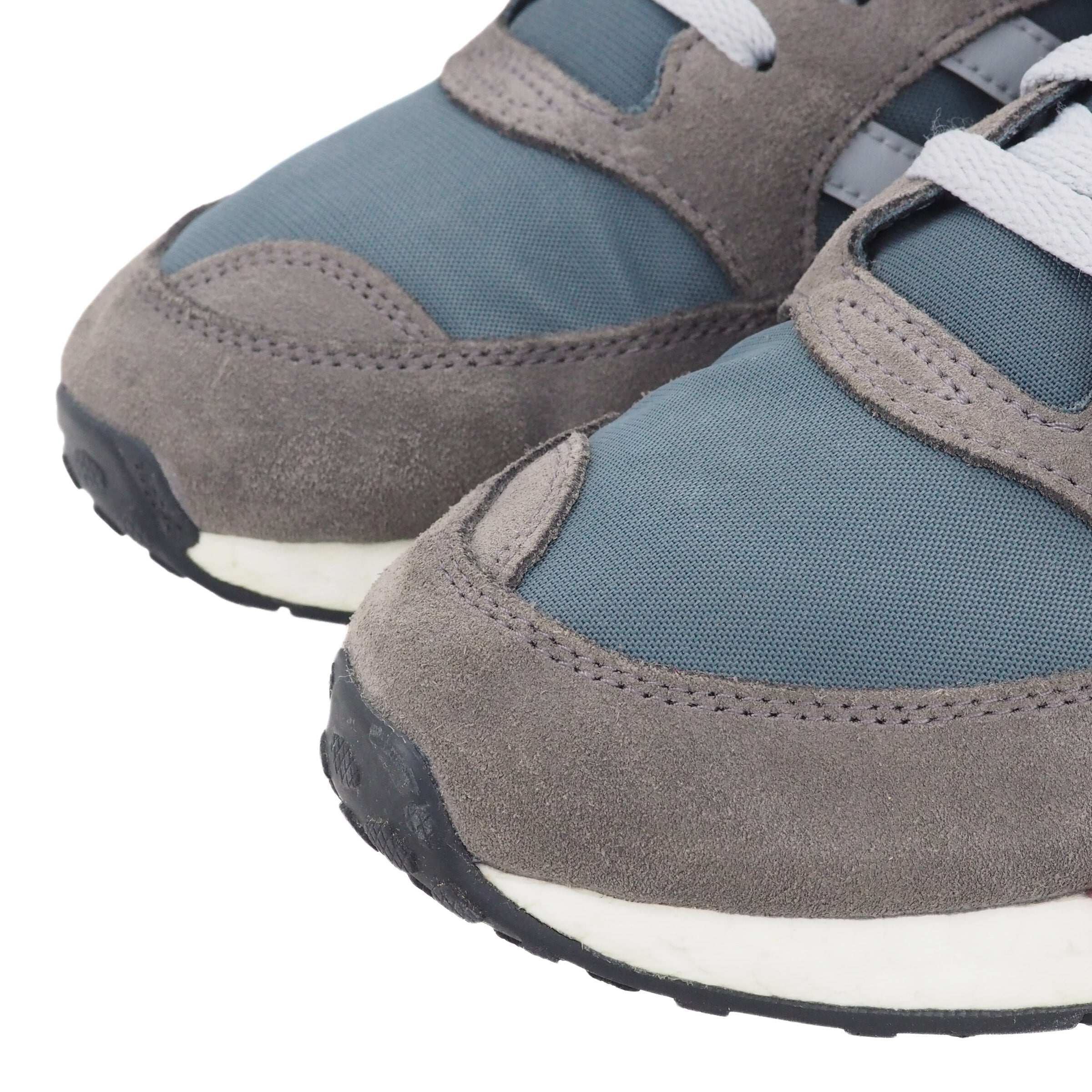 Close up of the toe area of a pair of gray and blue sneakers on a white background