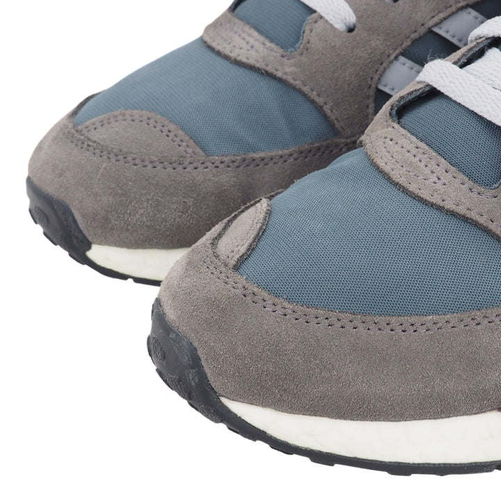 Close up of the toe area of a pair of gray and blue sneakers on a white background