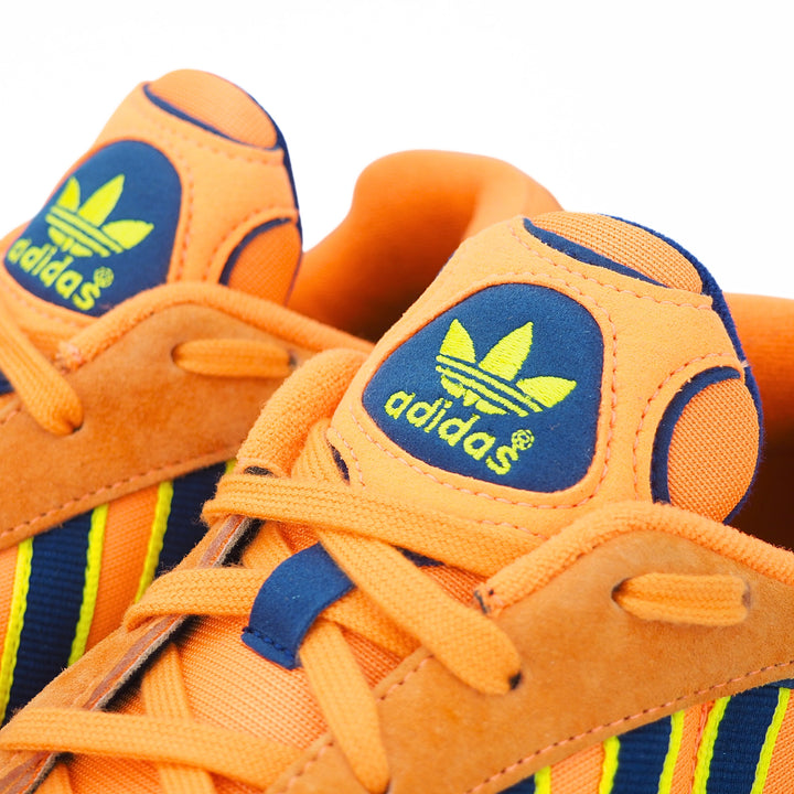 Close-up of the laces and tongue of a pair of orange Adidas sneakers with blue and yellow accents on a white background