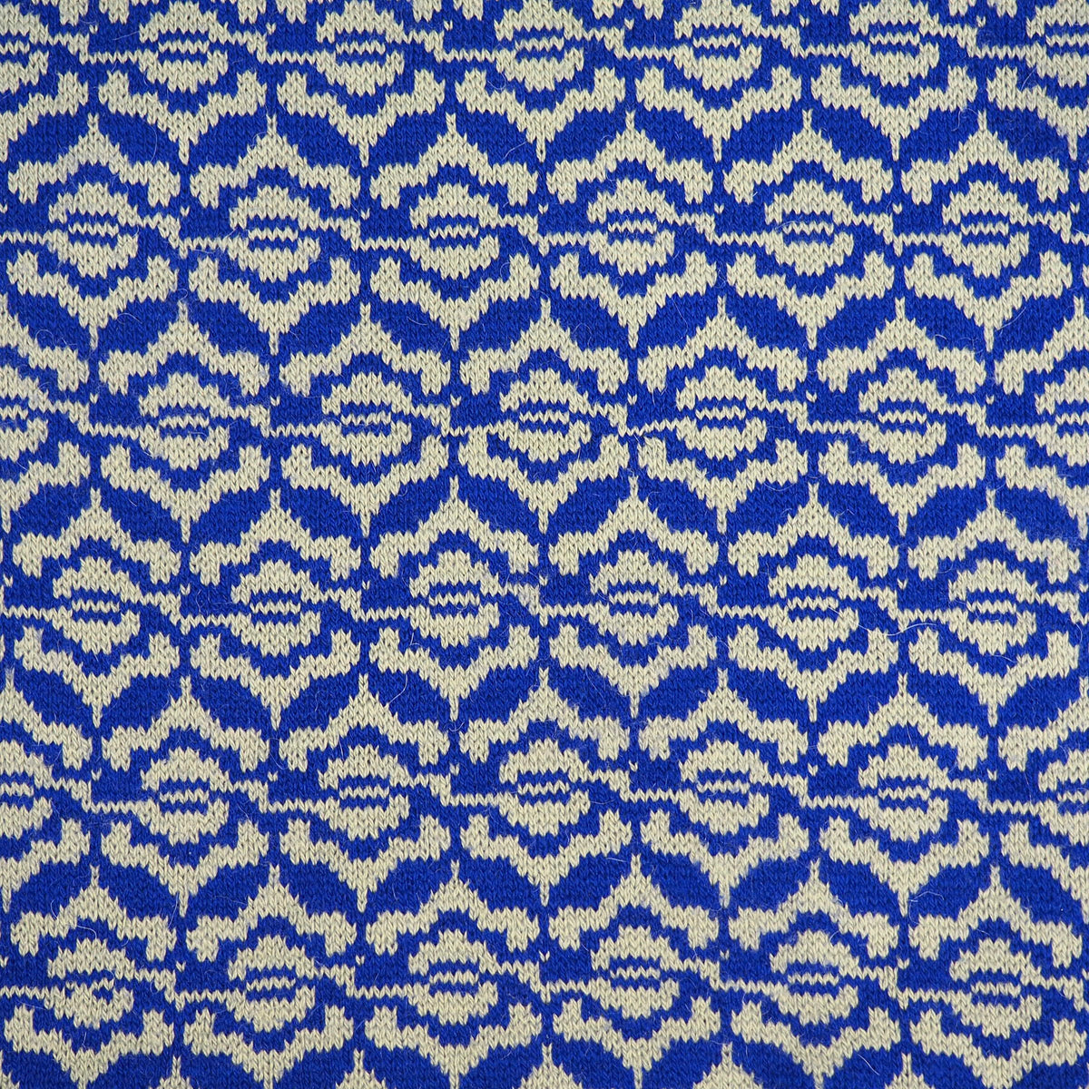 A close-up of a knitted fabric with a repeating geometric pattern in royal blue and grey.