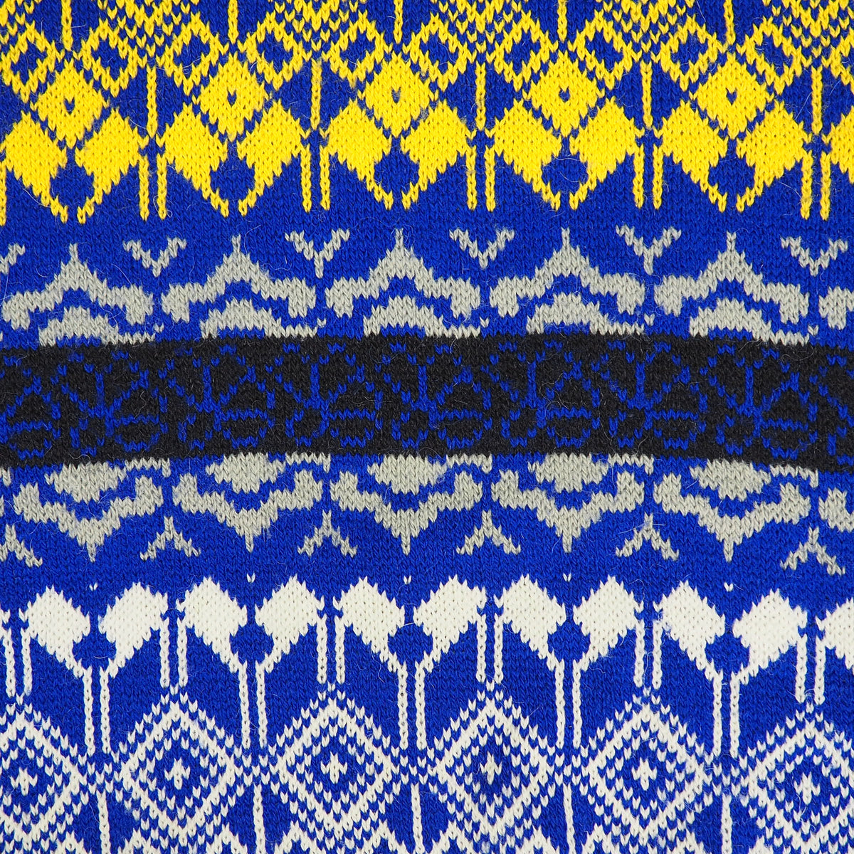 A close-up of a knitted textile with a Nordic pattern in royal blue, bright yellow, white, and a black horizontal band.