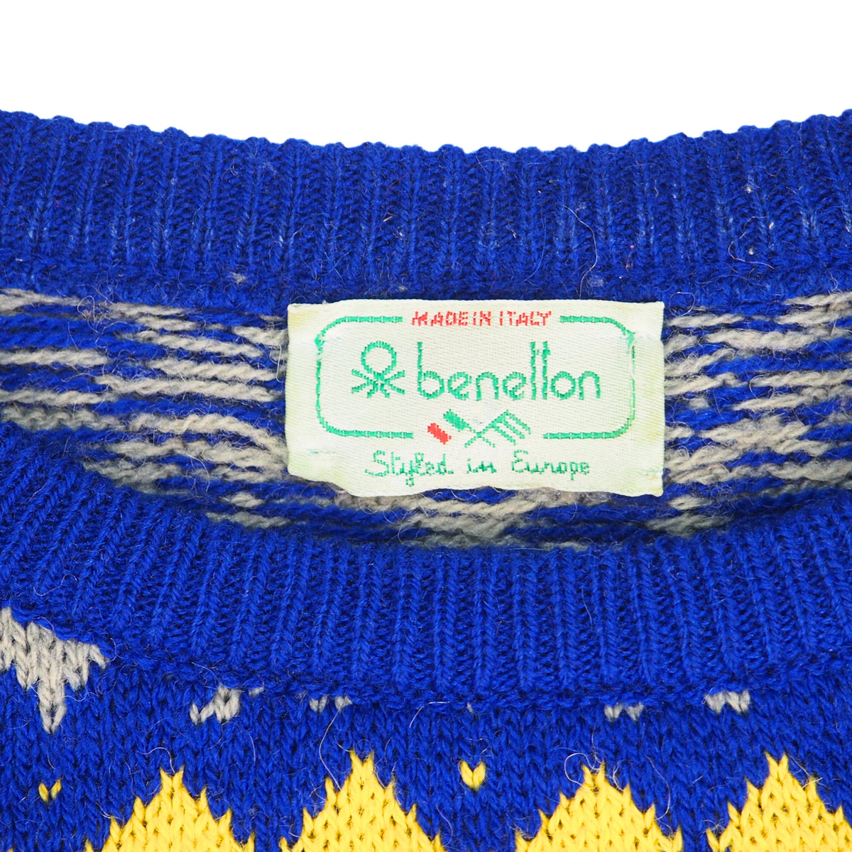 Close up of a blue, yellow and grey knitted wool sweater neck showing the manufacturer label which reads 'Benetton Styled in Europe'.