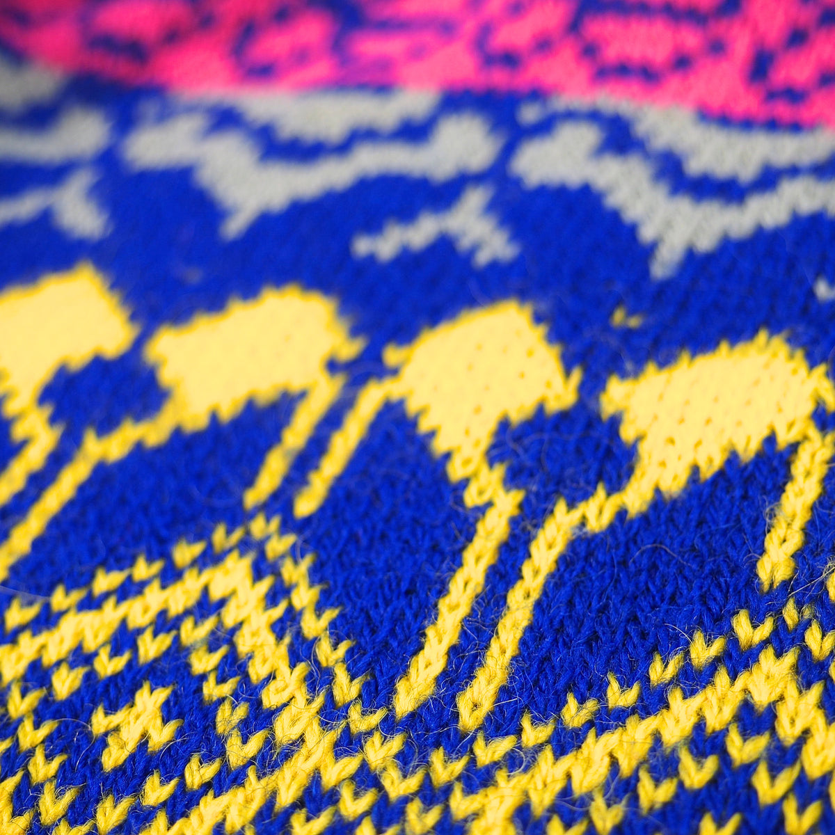 Close-up of a knitted textile with a bold pattern in royal blue, bright yellow, and pink, showing the knit texture and color blocking.
