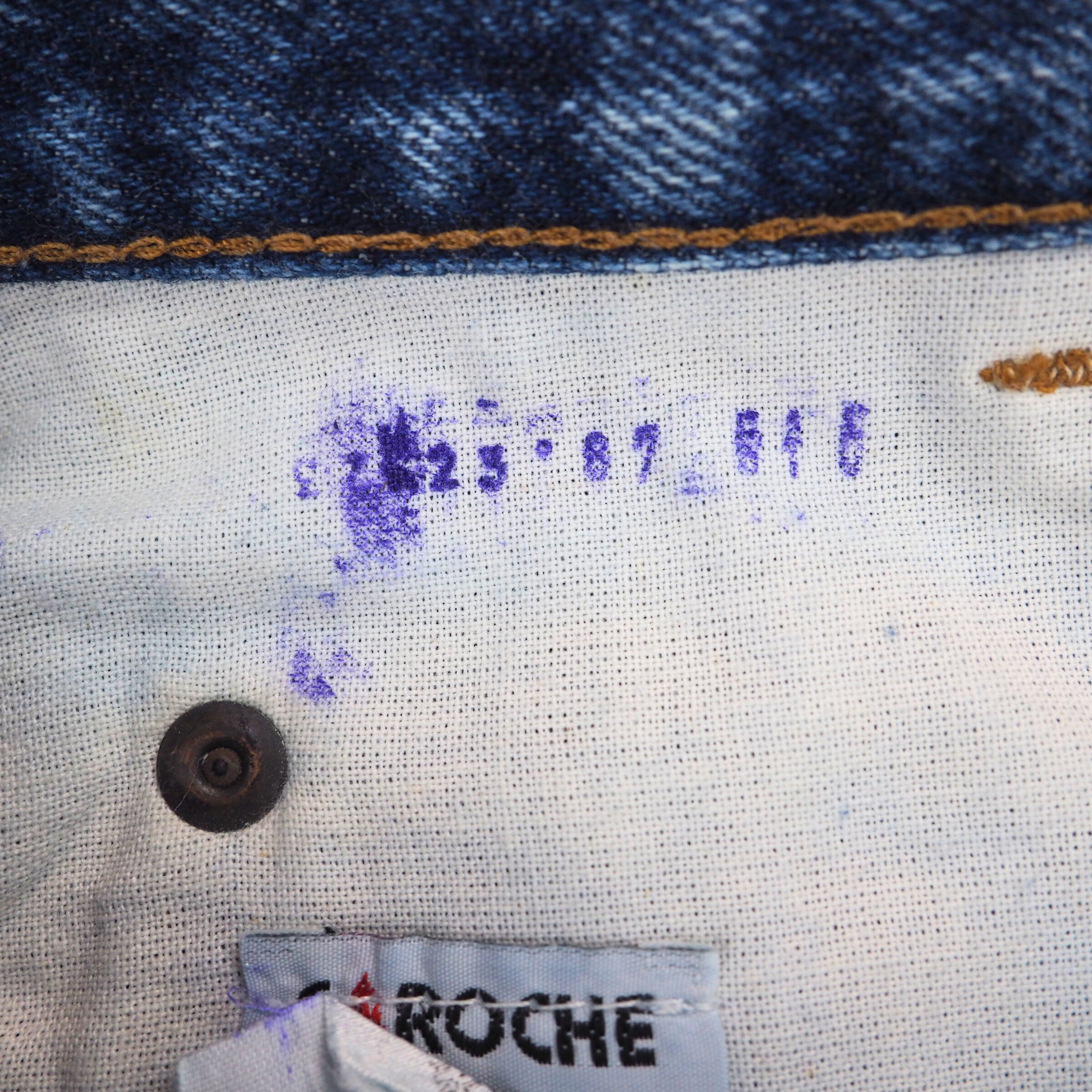 Close-up of a denim fabric and interior lining with a rivet and care label, featuring the brand 'Caroche'.