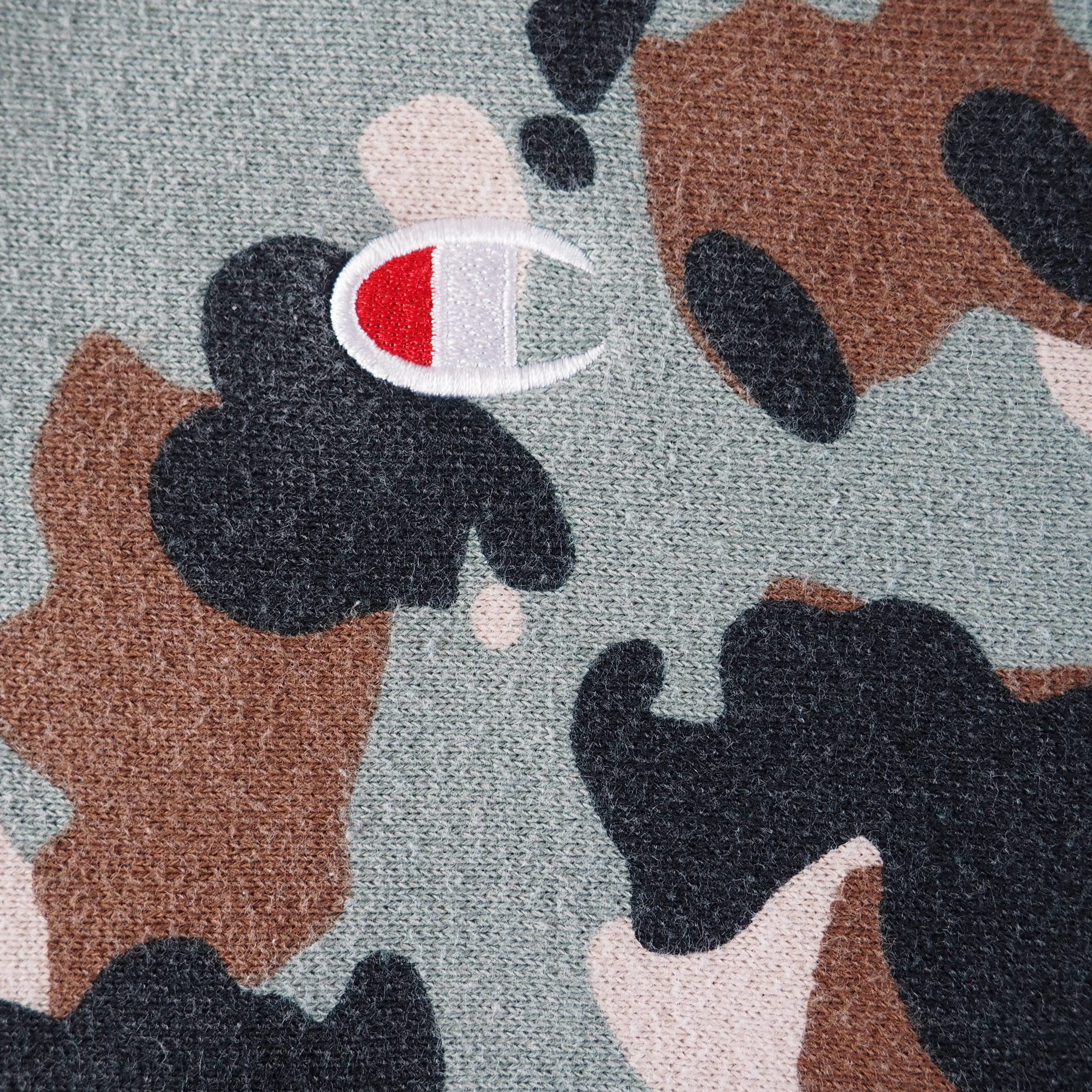 Close-up of a camouflage pattern with a Champion 'C' brand logo on a textured fabric background