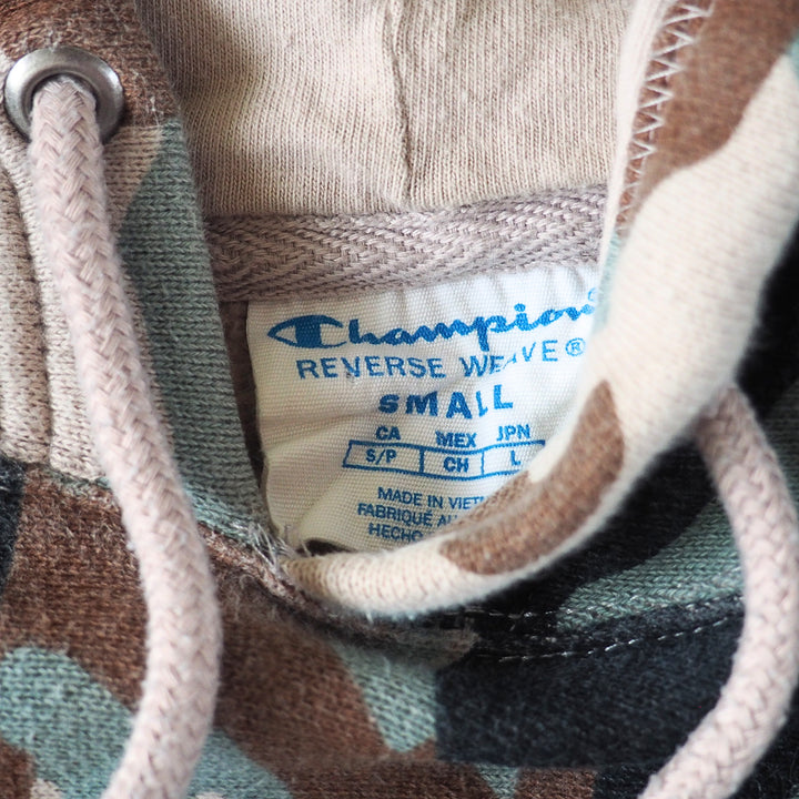 Close-up of a Champion 'Reverse Weave' label on the inside collar of a camouflage-patterned hoodie.