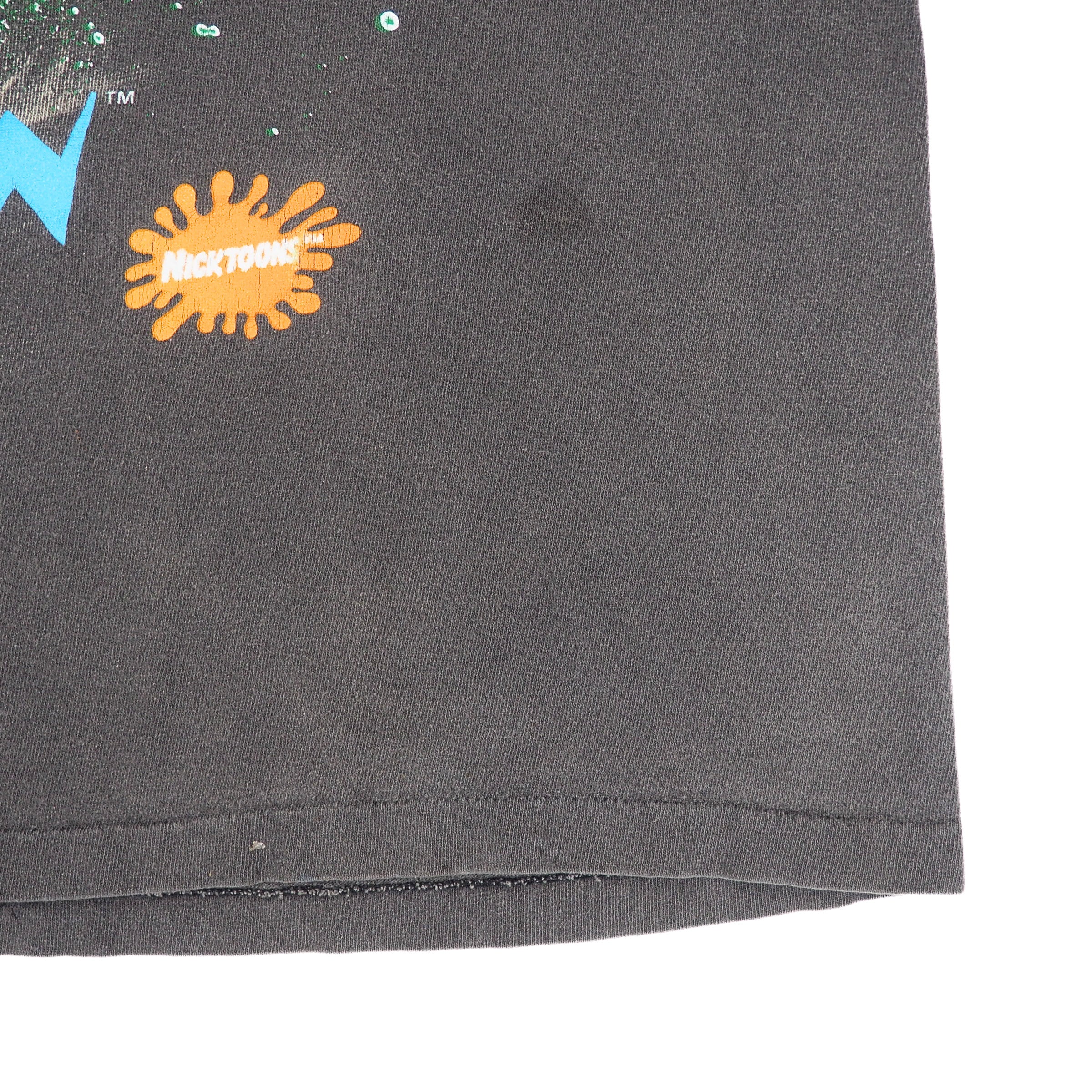 Close-up of a dark gray or black fabric surface with a visible orange splatter-style Nickelodeon logo and part of a blue graphic at the upper left, photographed against a white background.