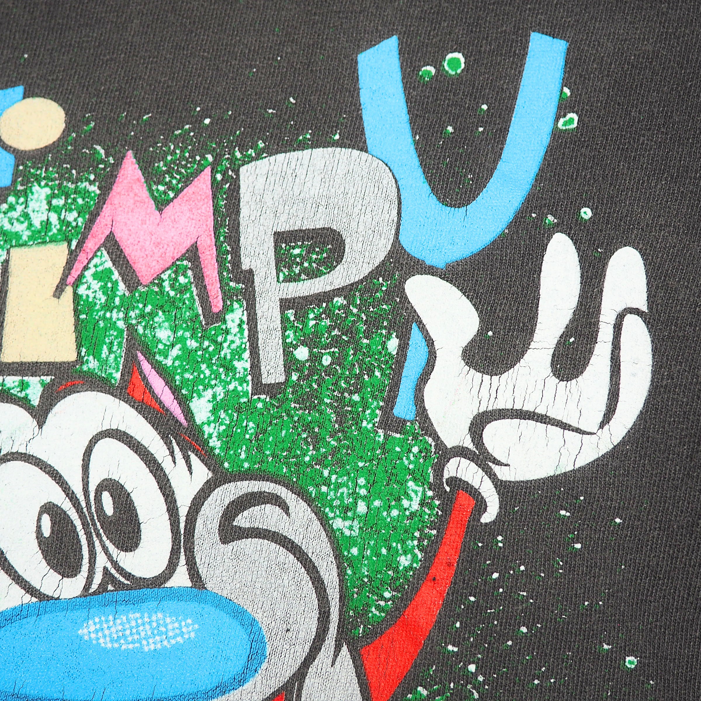 Close-up of a graphic print featuring a stylized face and hand in beige, red, pink, and white, set against a textured green and white splatter background on a dark base.