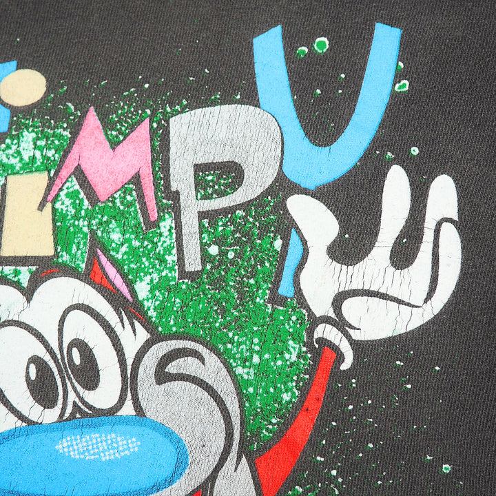 Close-up of a graphic print featuring a stylized face and hand in beige, red, pink, and white, set against a textured green and white splatter background on a dark base.