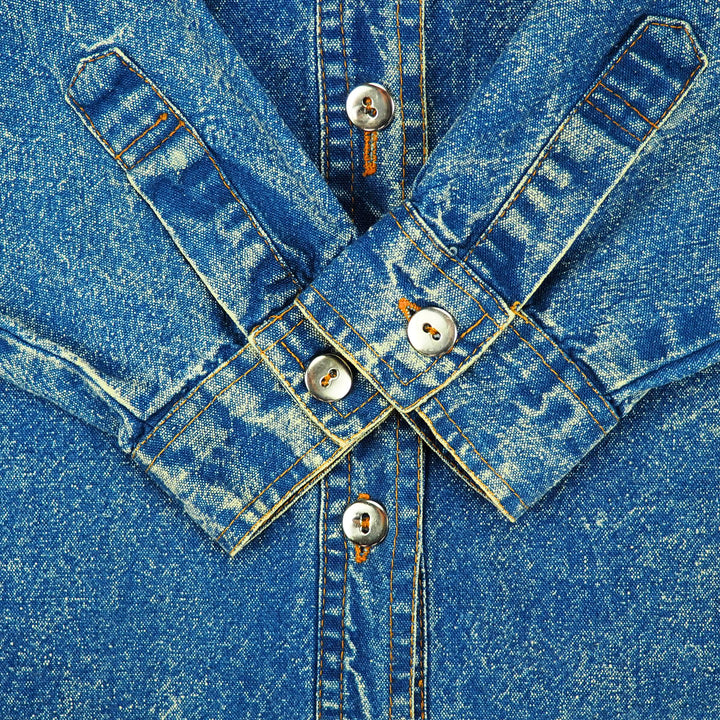 Close-up of a blue acid wash denim sleeve cuffs folded with metallic silver buttons folded onto the body of the shirt