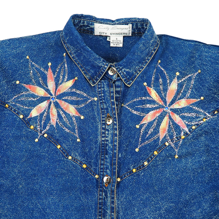Blue denim shirt with floral embroidery and decorative buttons on a white background