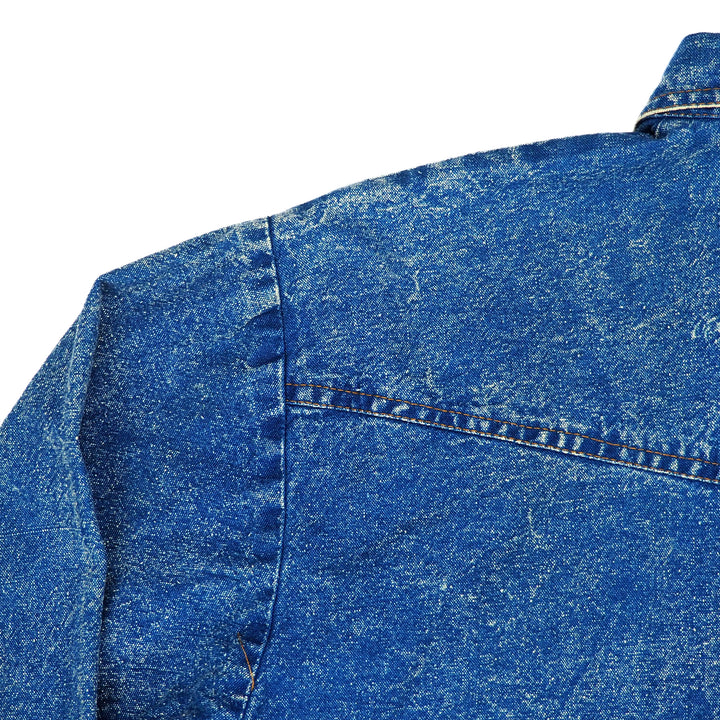 Close-up of a blue denim shirt jacket left rear shoulder on a white background