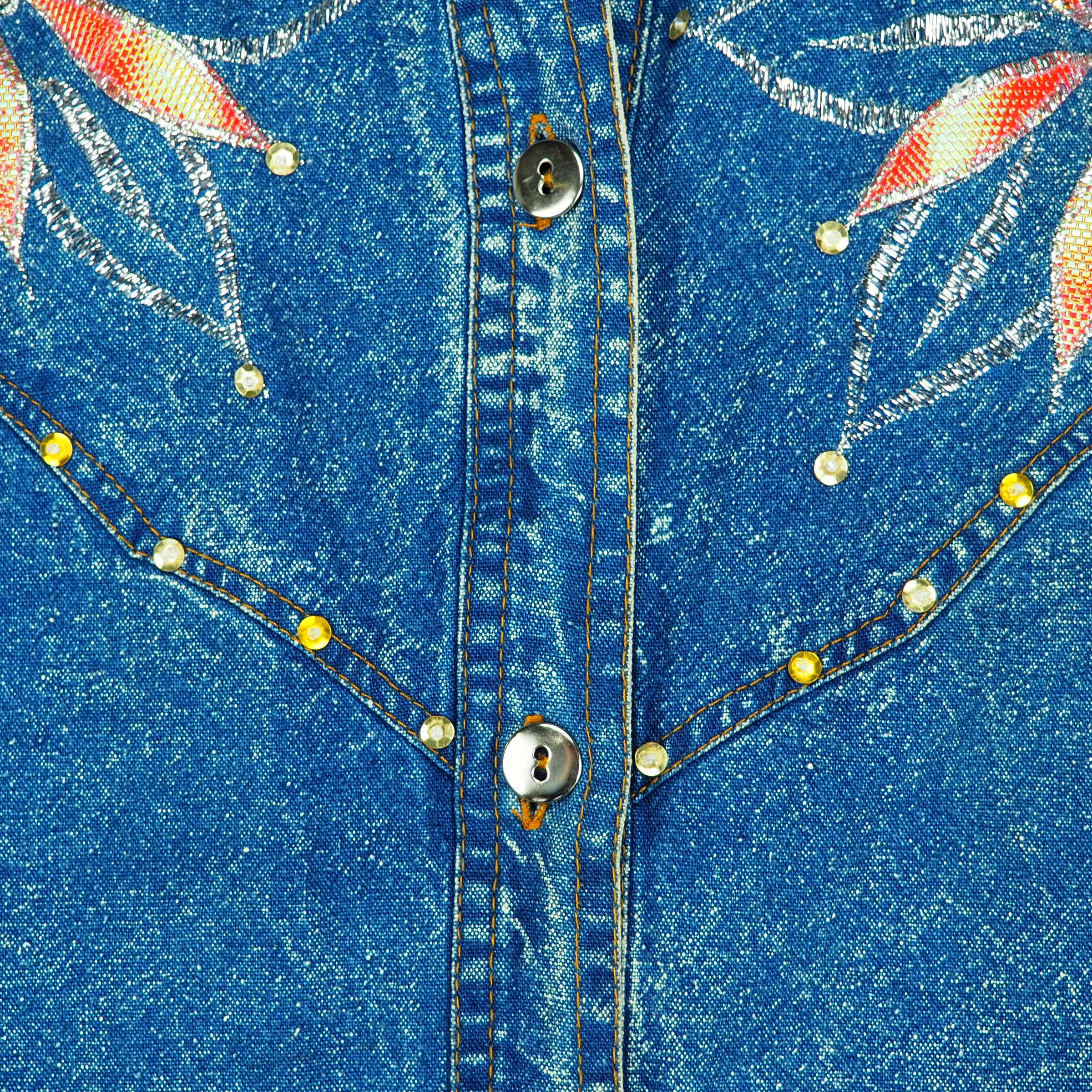 Close-up of a blue denim shirt with floral embroidery and decorative buttons.