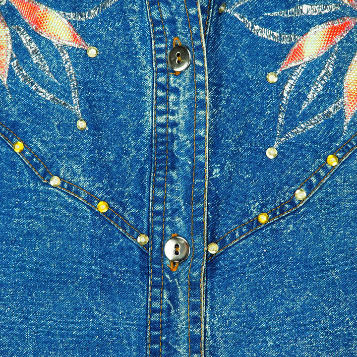 Close-up of a blue denim shirt with floral embroidery and decorative buttons.
