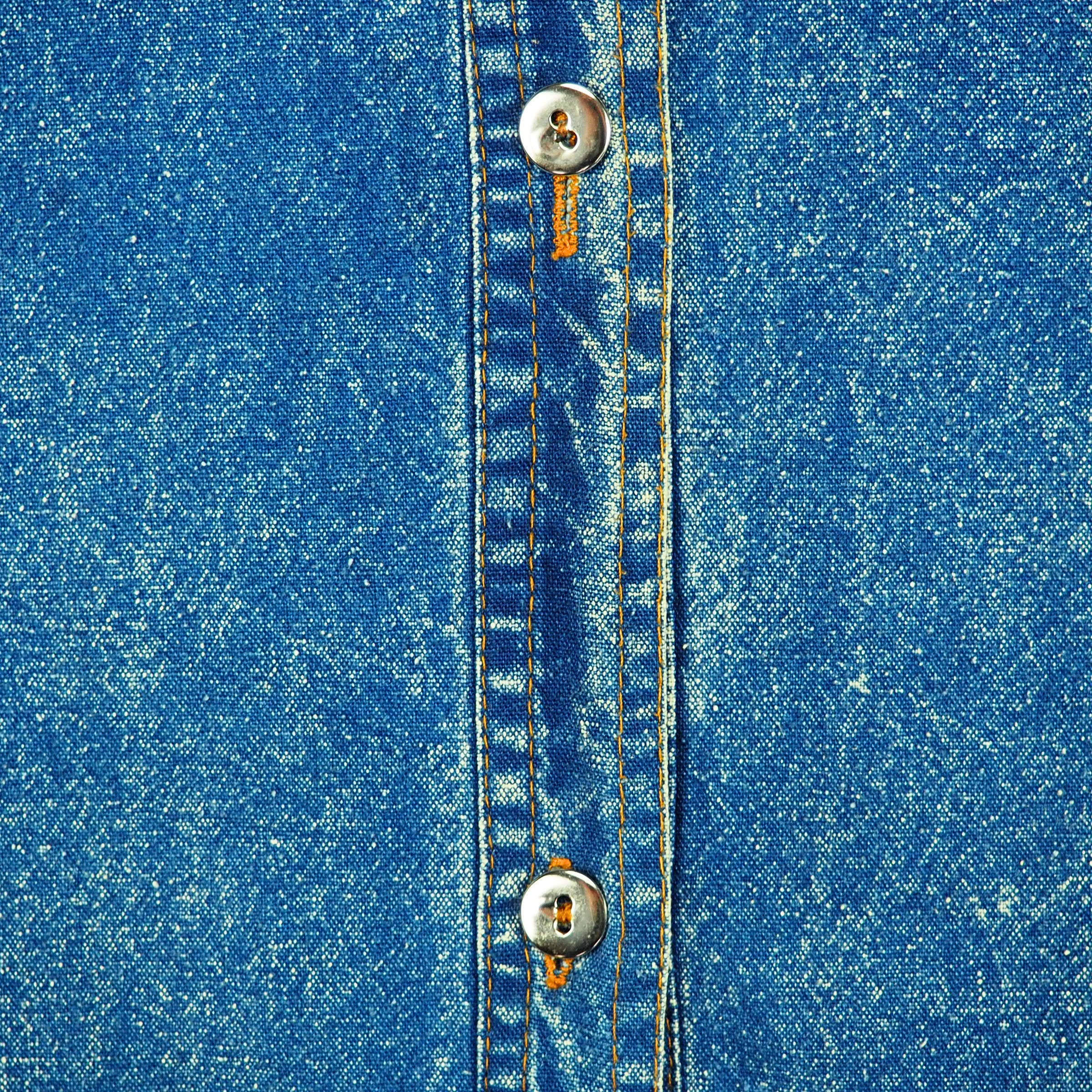 Close-up of blue denim fabric with metallic silver buttons and orange stitching