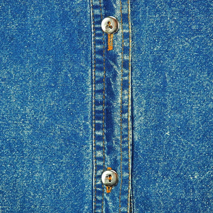 Close-up of blue denim fabric with metallic silver buttons and orange stitching