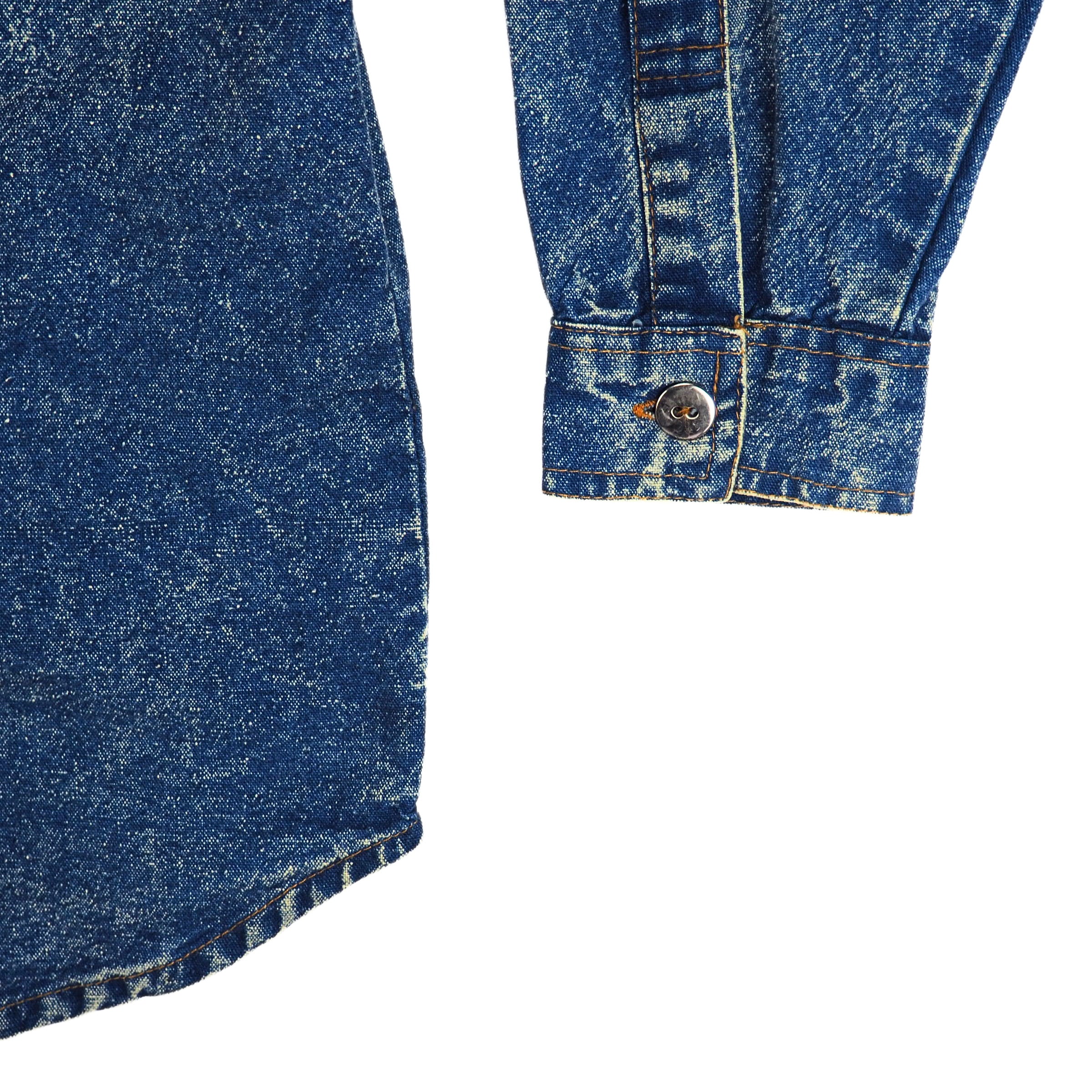 Close-up shirt tail and sleeve cuff detail of a blue acid wash denim shirt on a white background