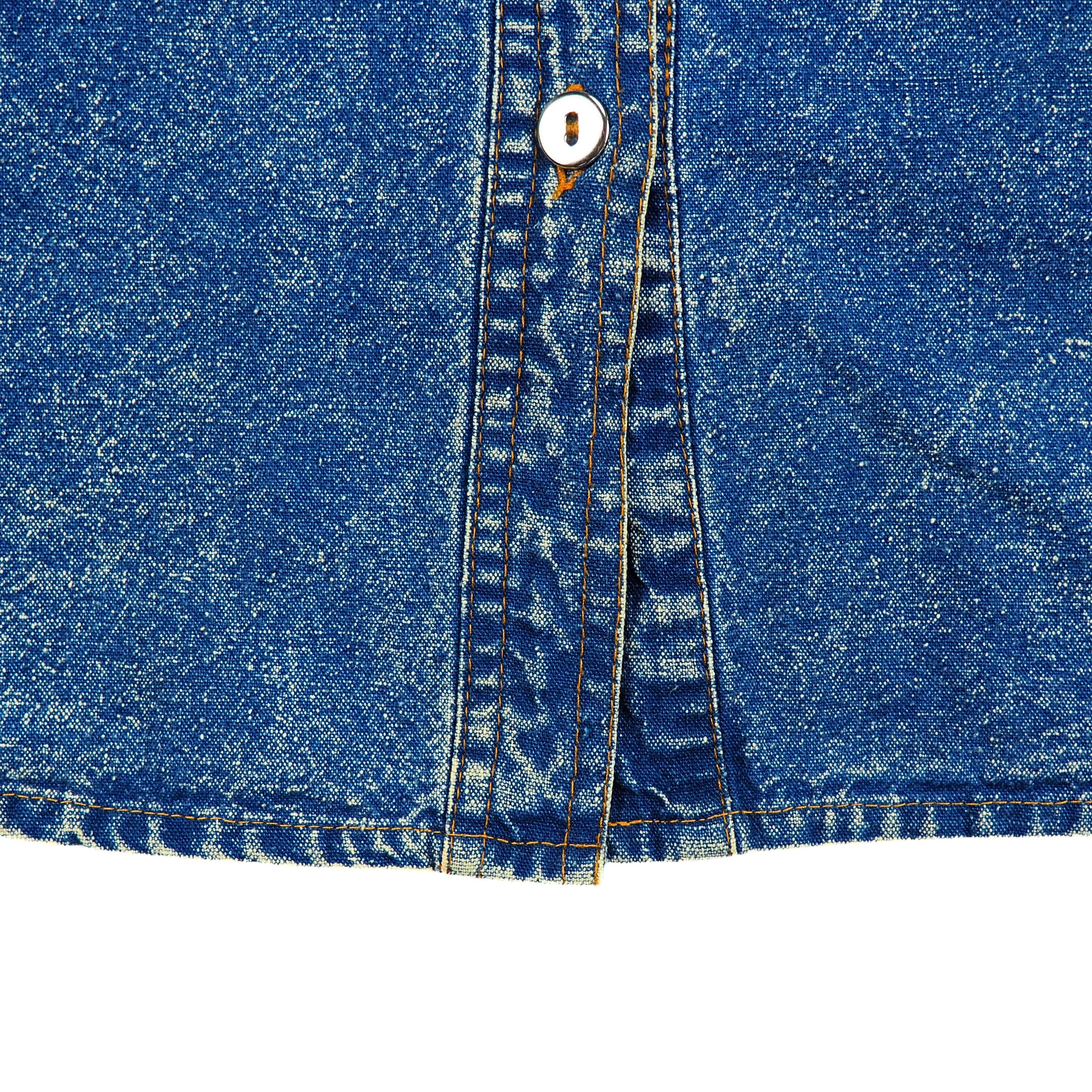 Close-up of blue denim fabric with a metallic silver button on a white background