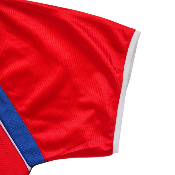 Close-up of a soccer jersey sleeve, red fabric with blue and white trim on a white background