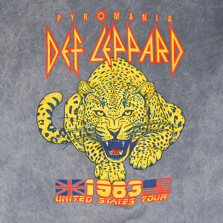 Close up of a graphic logo on a faded grey t-shirt reading 'PYROMANIA DEF LEPPARD 1983 US TOUR' with an image of a leopard in red, yellow and blue screen print.