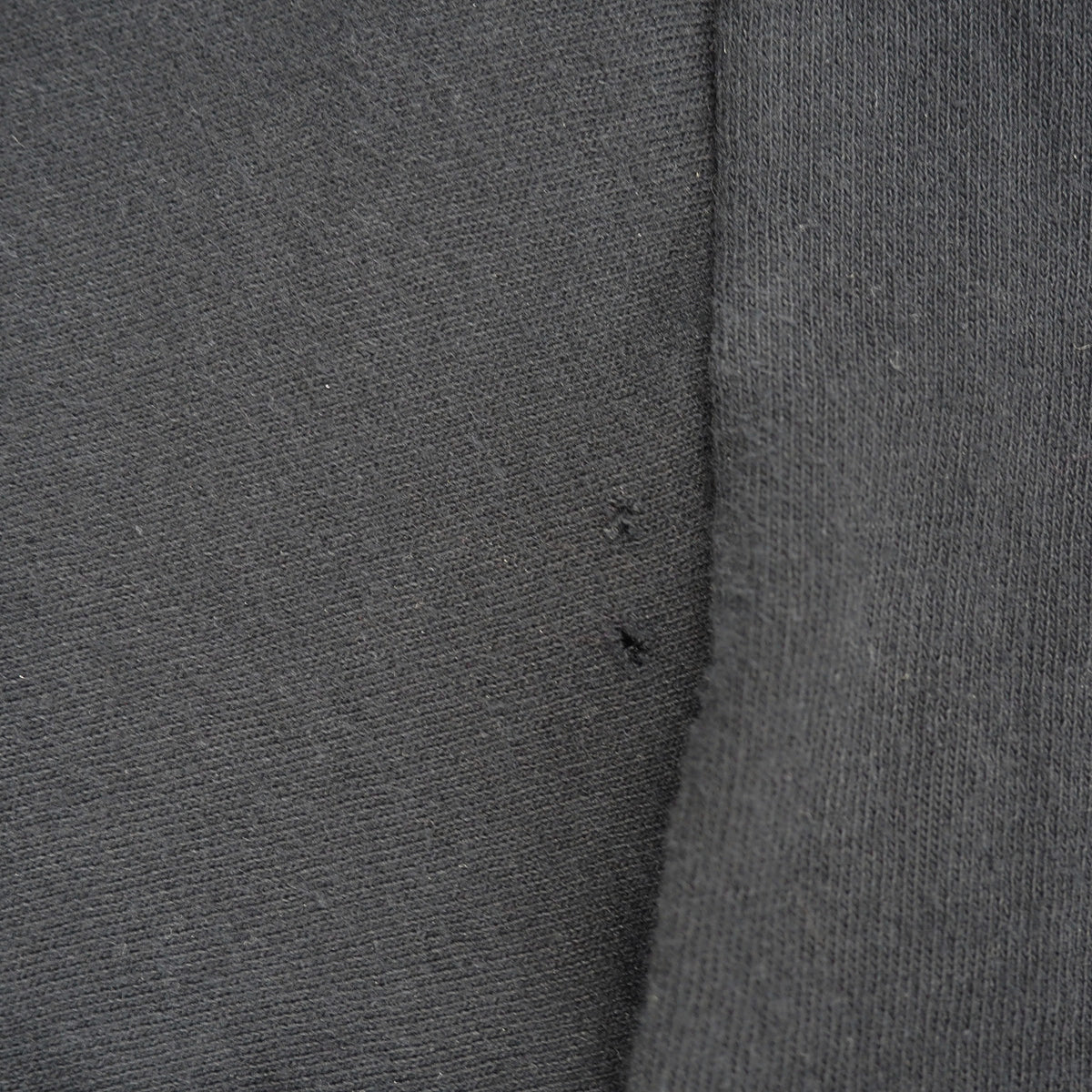 Close-up of dark gray knit fabric with a visible seam and two small dark thread ends.