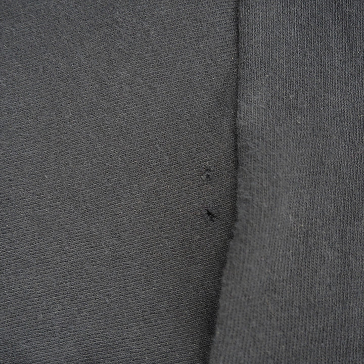 Close-up of dark gray knit fabric with a visible seam and two small dark thread ends.