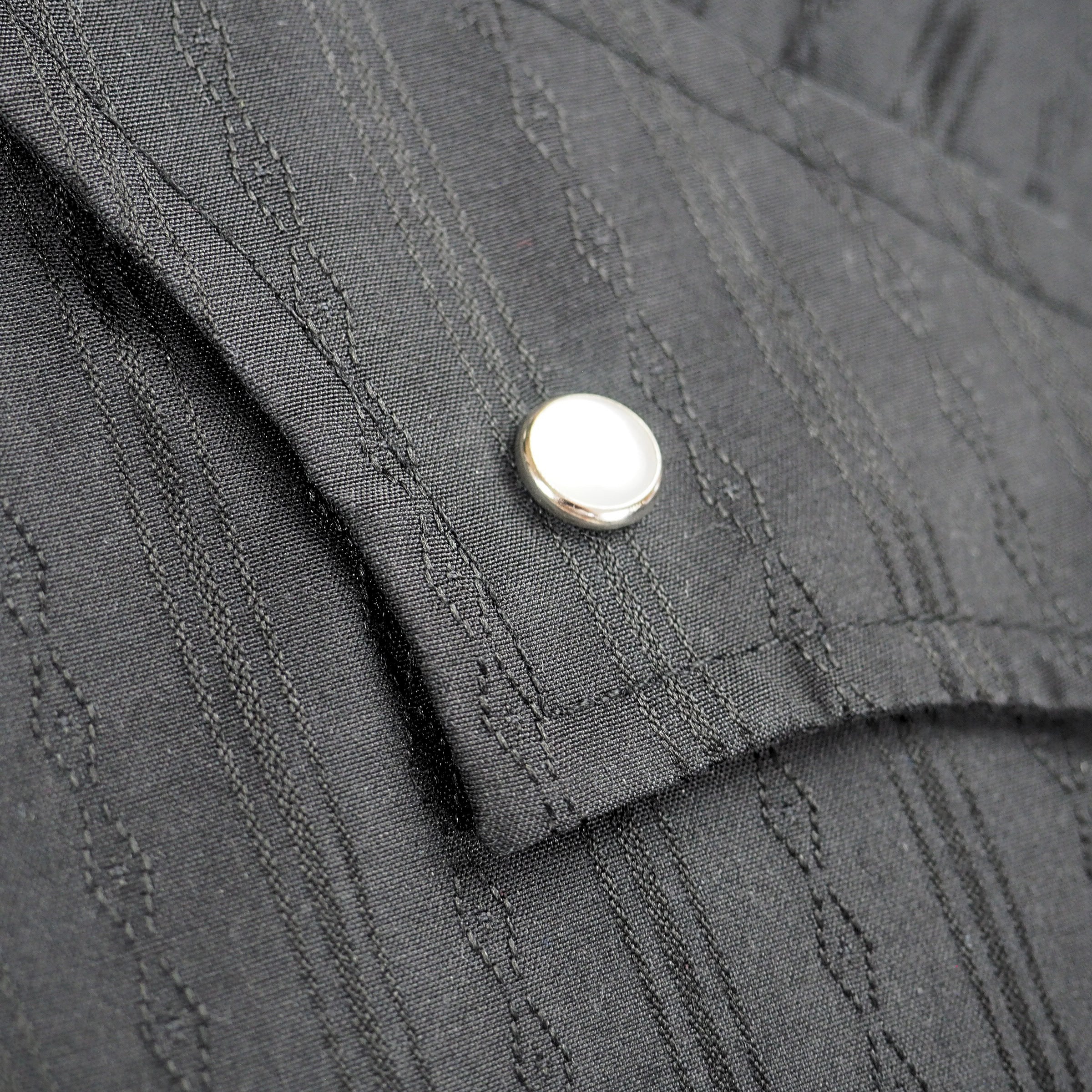Close up of the pocket flap and pearl snap press stud of a black dress shirt in a western style.