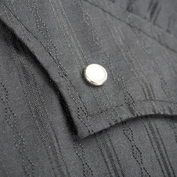 Close up of the pocket flap and pearl snap press stud of a black dress shirt in a western style.