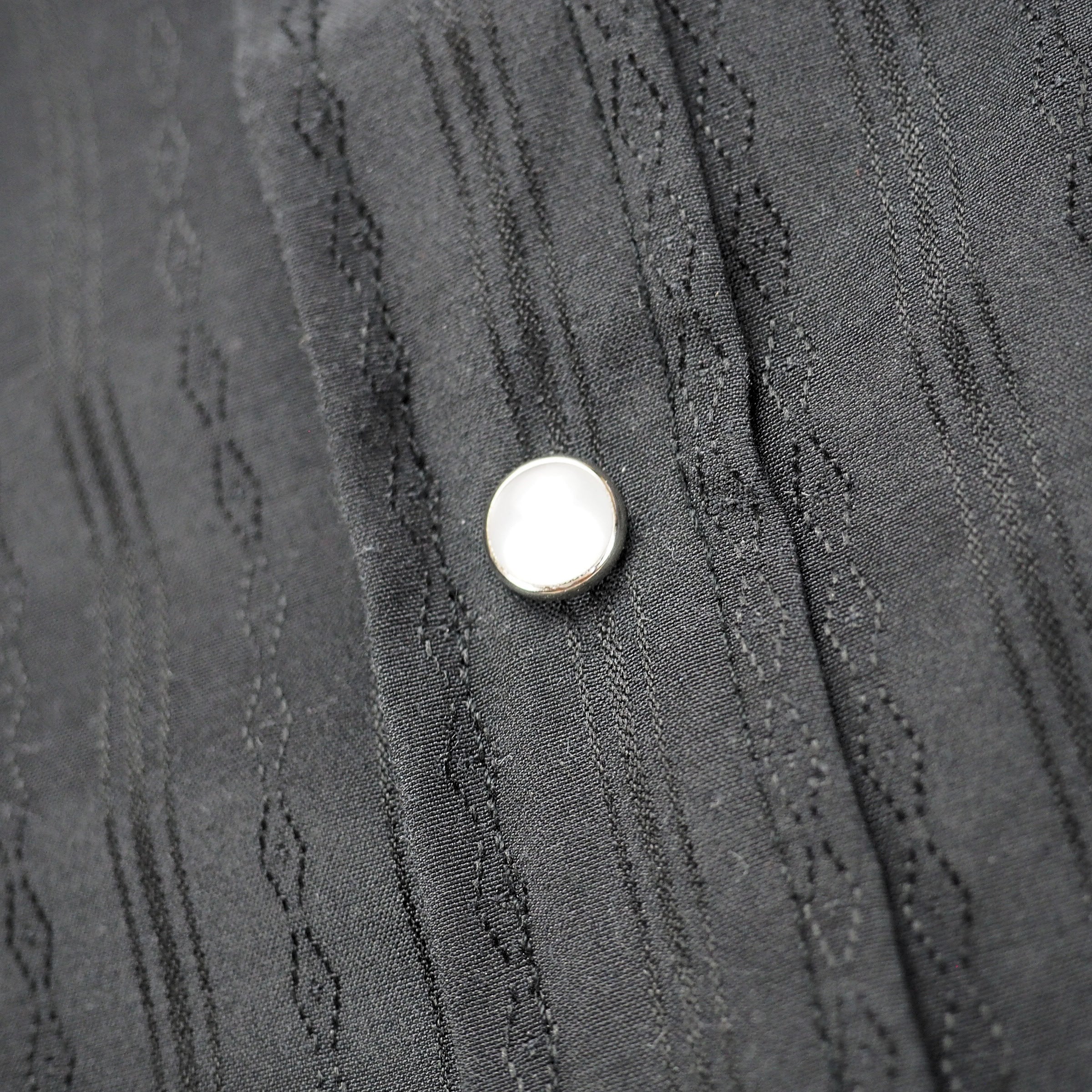 Close up of pearl snap press stud on a back patterned shirt placket.