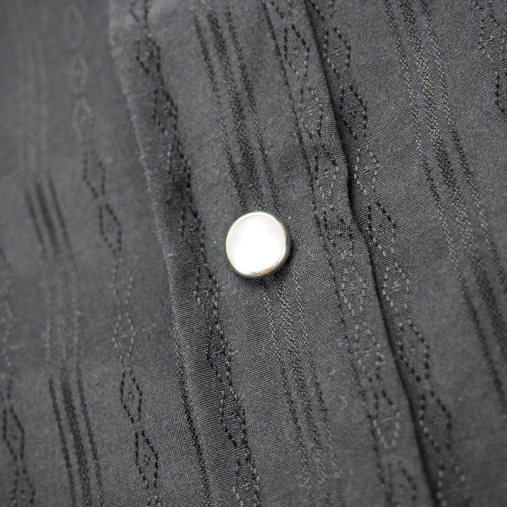 Close up of pearl snap press stud on a back patterned shirt placket.
