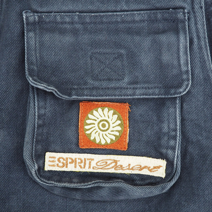 Close-up of a denim garment pocket with a square orange patch featuring a white flower and a white embroidered 'ESPRIT DESERT' label below it.