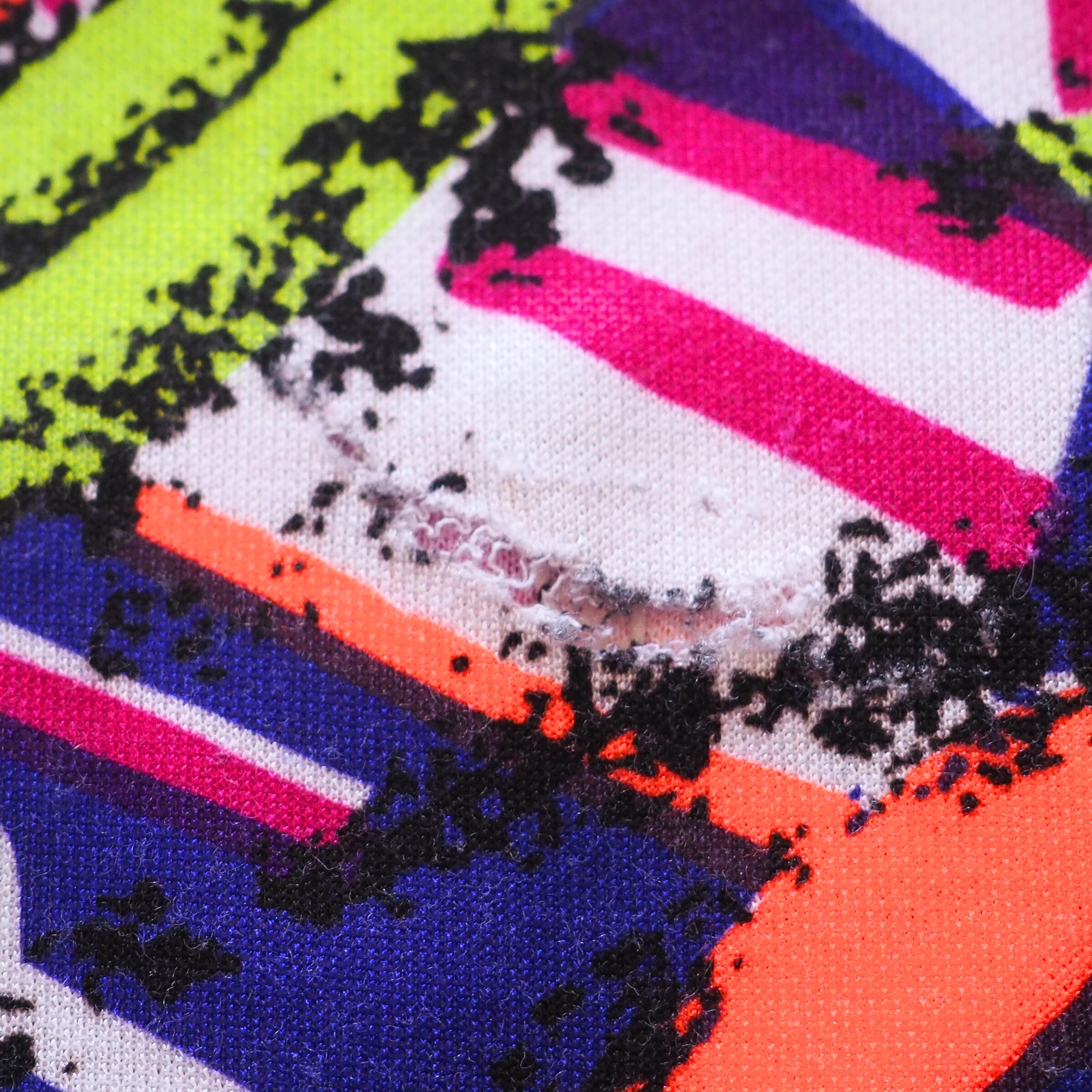 Close-up of a colorful jersey with geometric patterns and black specks and detailing a small tear in the fabric