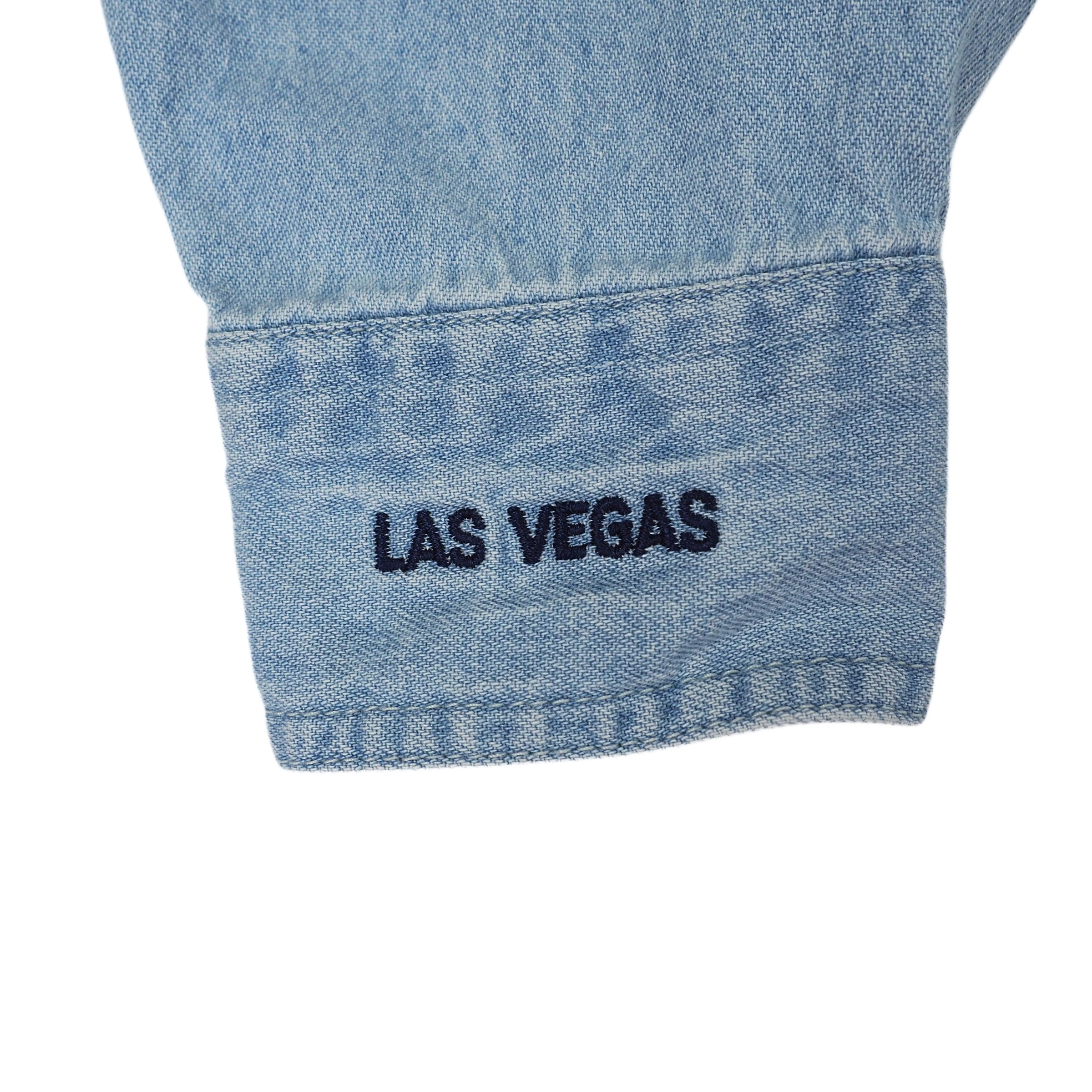 Close-up of a blue denim shirt sleeve cuff with 'Las Vegas' embroidery on a white background