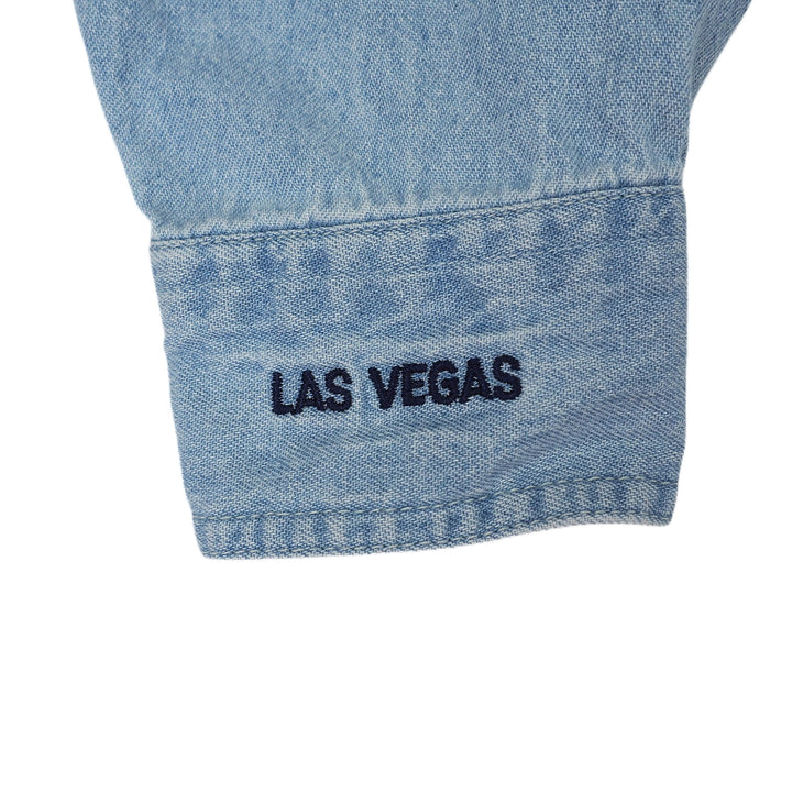Close-up of a blue denim shirt sleeve cuff with 'Las Vegas' embroidery on a white background