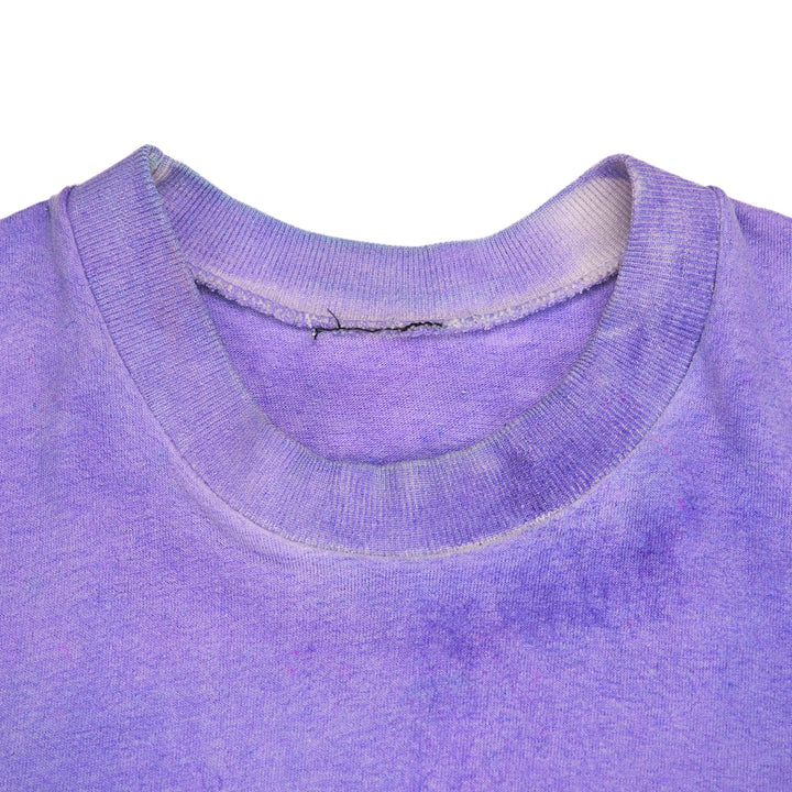 Close-up of a purple crewneck t-shirt showing the ribbed collar and a subtle faded purple wash on the front, set against a plain white background.