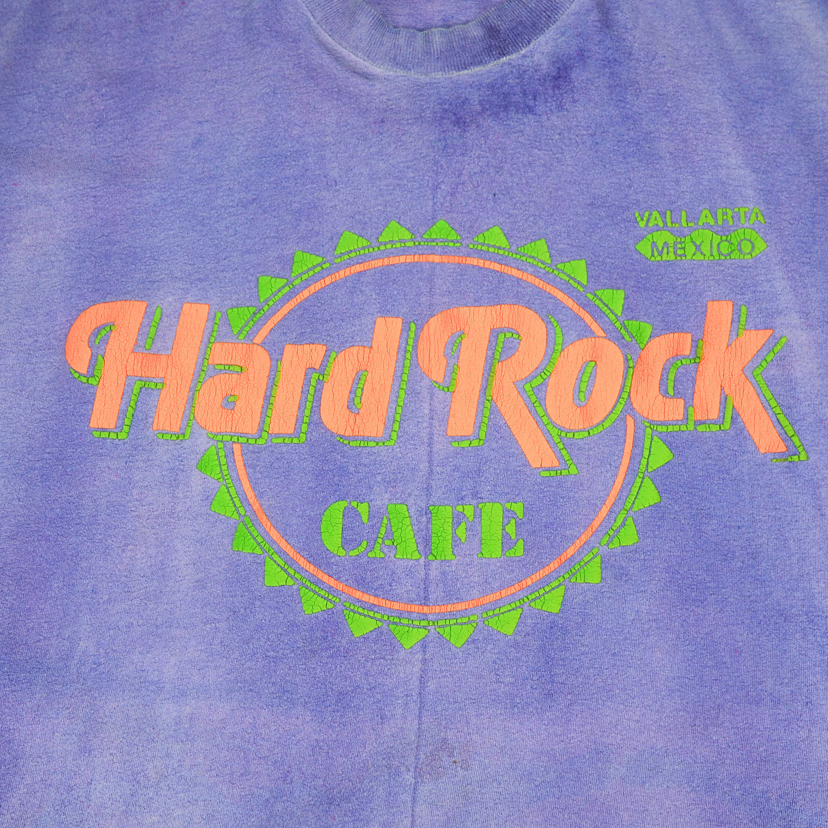 A close-up of a purple tie-dye t-shirt featuring the 'Hard Rock CAFE' logo in orange and green on the chest, with 'VALLARTA MEXICO' printed in green on the upper right.