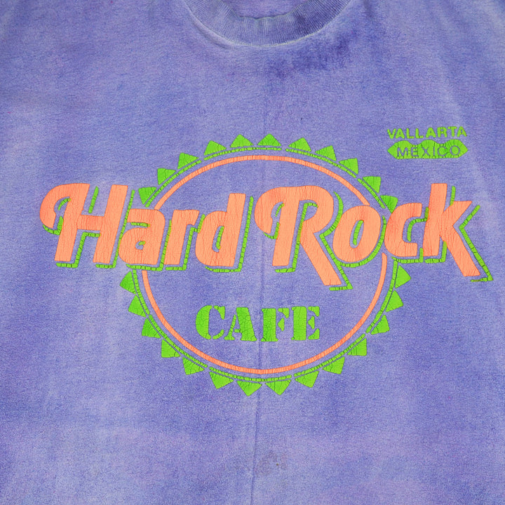A close-up of a purple tie-dye t-shirt featuring the 'Hard Rock CAFE' logo in orange and green on the chest, with 'VALLARTA MEXICO' printed in green on the upper right.