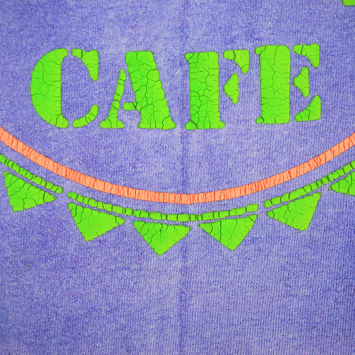 Close-up of a purple knit fabric with bright green puff-print letters spelling "CAFE" and a curved orange line and green arrow heads below.