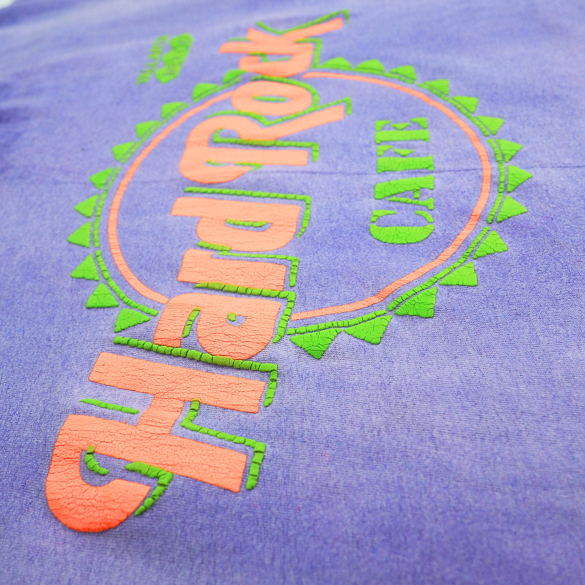 A close-up of a purple t-shirt featuring a large, colorful embroidered Hard Rock Cafe logo in orange and green.