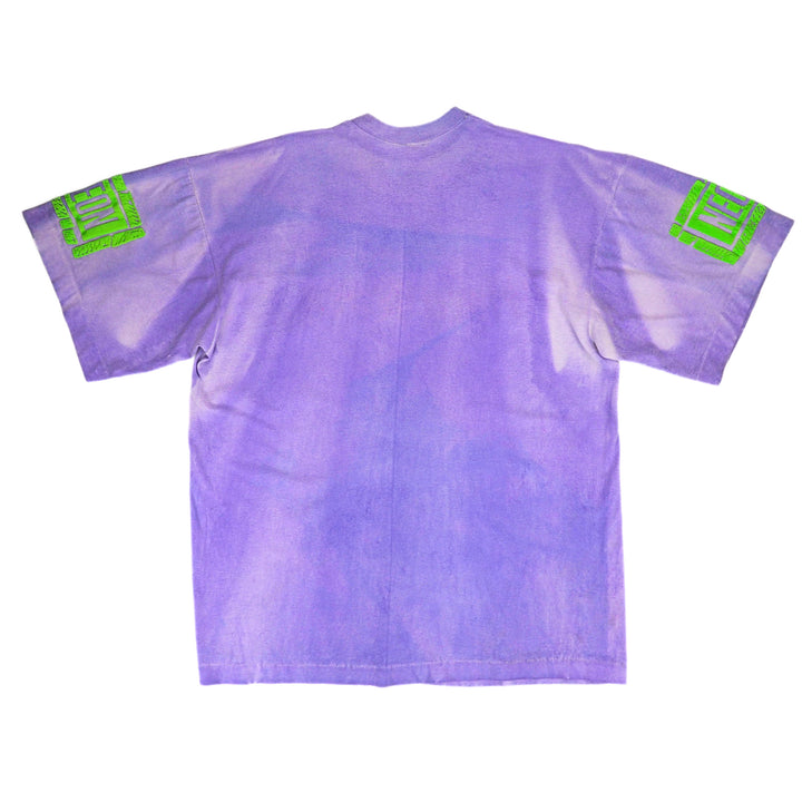 A light purple short-sleeve t-shirt shown from the back, featuring a subtle vertical tie-dye or watercolor effect and bright green graphic patches on both sleeves.