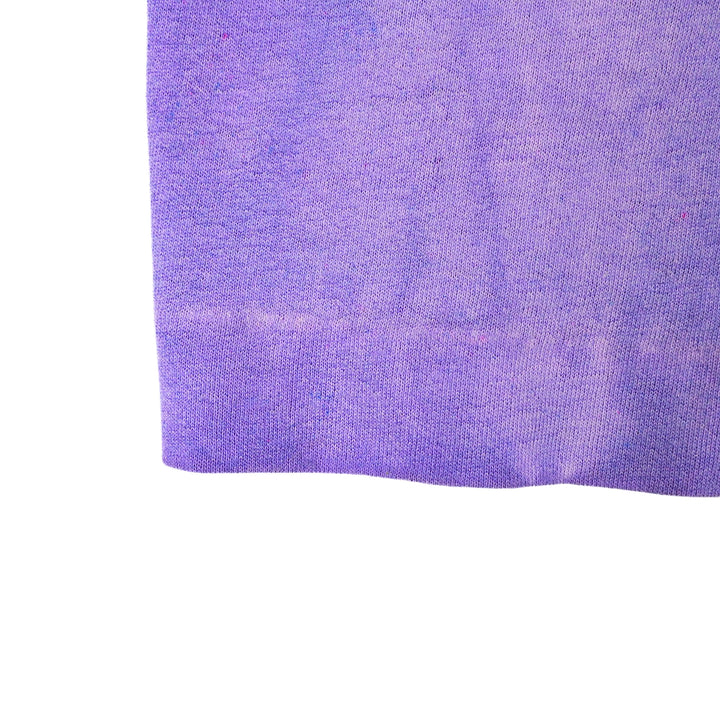 A close-up of a purple textured fabric, likely a knit sweater or jersey material, shown against a plain white background.