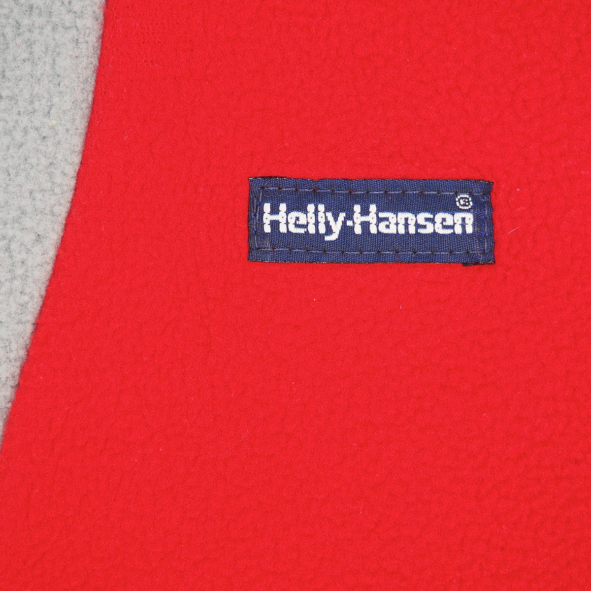 Close-up of a bright red fleece garment with a navy blue Helly-Hansen brand label sewn onto the chest.