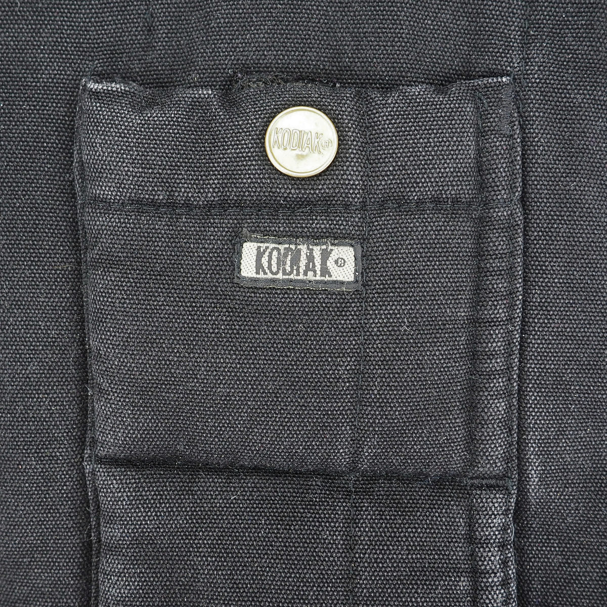 Close-up of a dark charcoal gray fabric pocket with a silver snap button and a white KODIAK brand label.