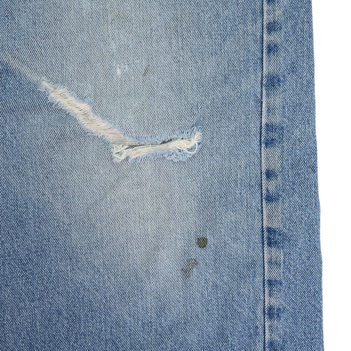 Close-up of a blue denim jeans knee area with a tear and stitching detail.