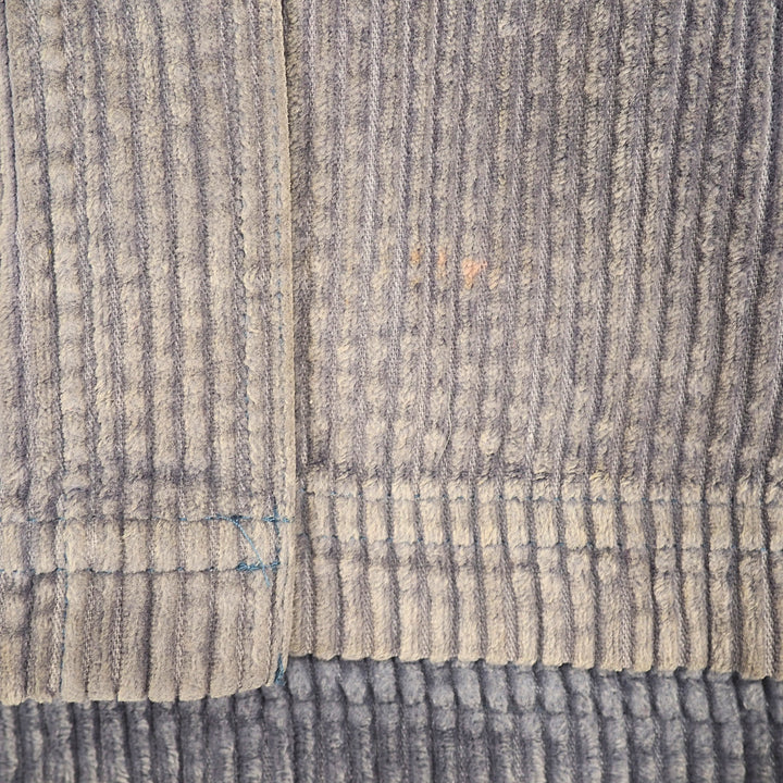 A close-up of a ribbed corduroy fabric in a heathered gray and beige colorway, showing the vertical ribbed texture and stitched edges.
