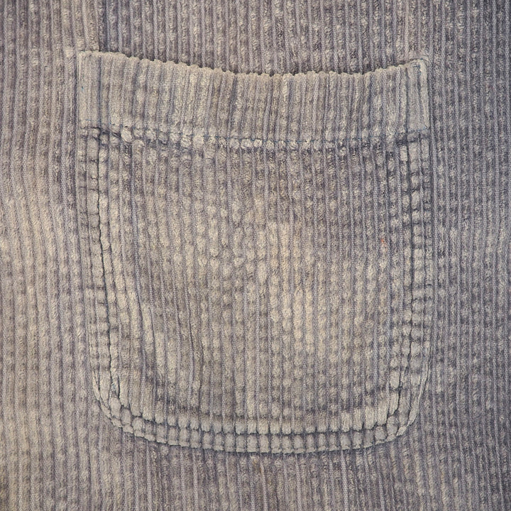 Close-up of a ribbed corduroy pocket in a muted grayish beige tone, showing the fabric texture and stitched edge.