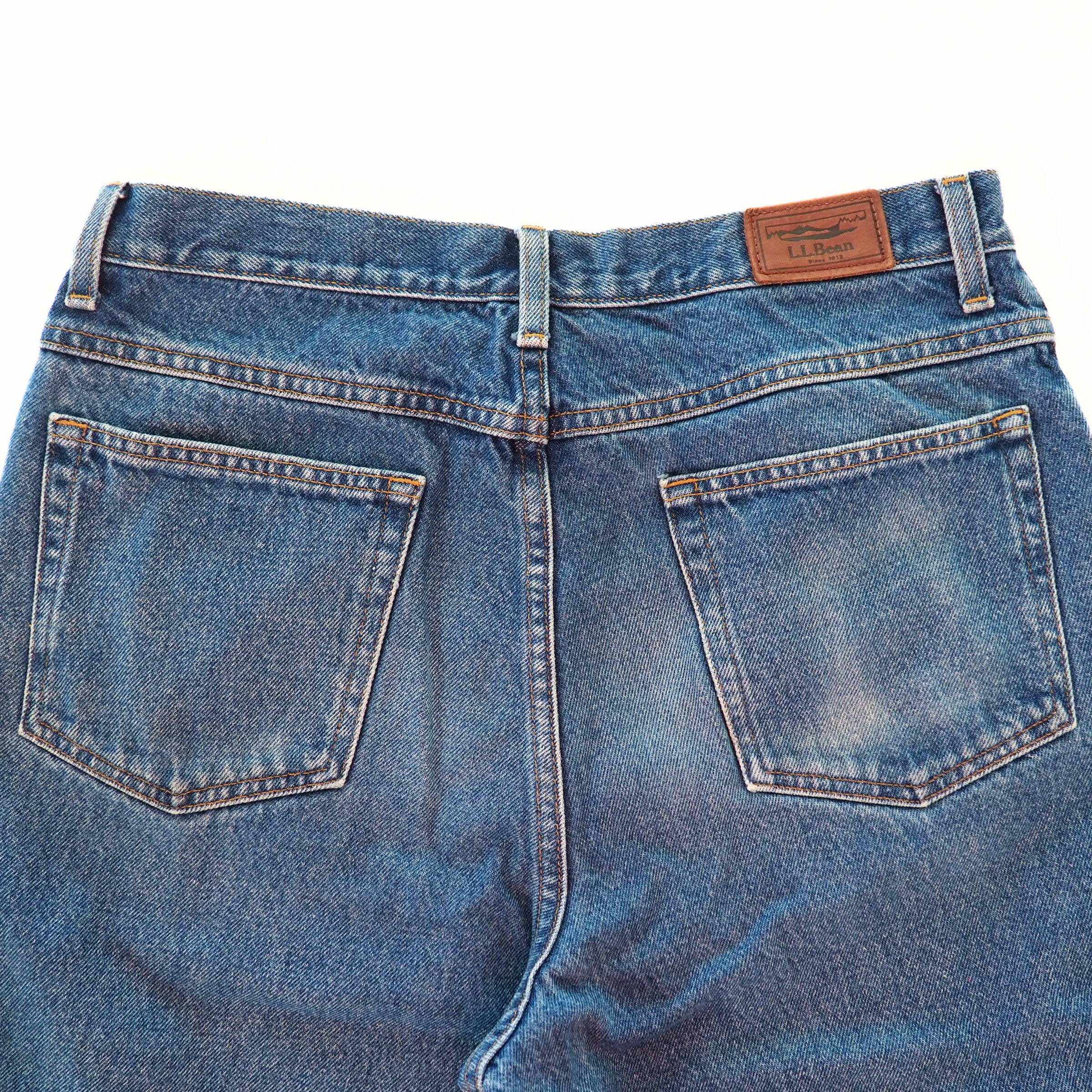 Back view focusing on the pockets of a pair of blue jeans with a brand label on a white background